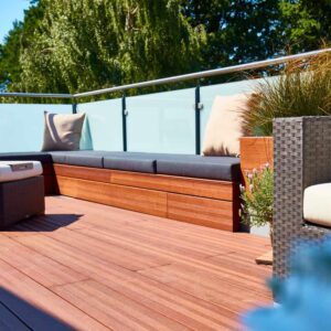 Entspannte Terrasse mit Holzdecks, Sitzkissen und Blick auf grüne Bäume im Hintergrund.
